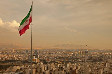 iran flag in the wind above skyline of tehran